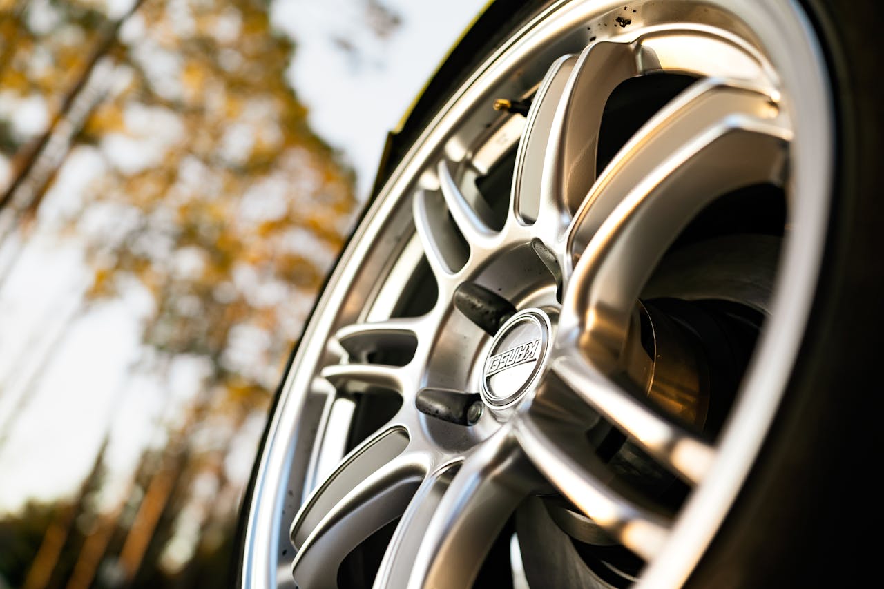 Detailed shot of a silver alloy wheel with blurred autumn trees in the background.